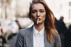 Free photo blonde girl with cigar stands on the street