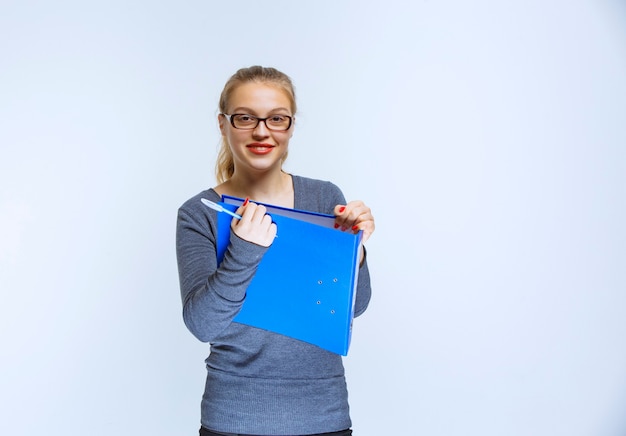 Blonde girl with eyeglasses holding a blue folder and smiling.