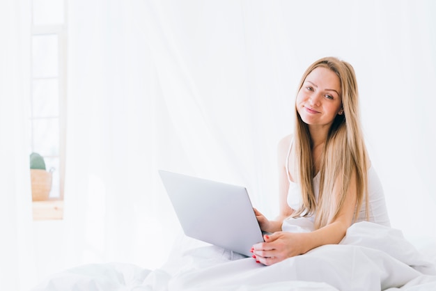 Blonde girl with laptop on the bed