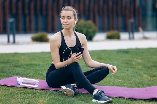 Blonde girl with ponytail sitting on yoga mat looking aside