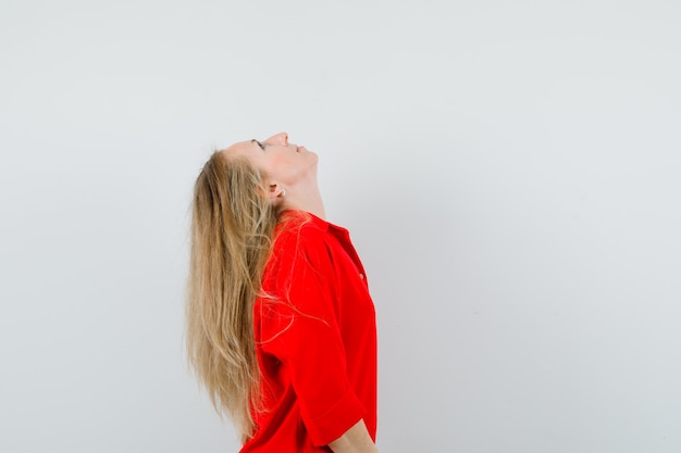 Blonde lady bending head back in red shirt and looking focused. .