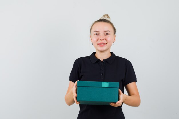 Blonde lady in black t-shirt holding present box and looking cheerful , front view.