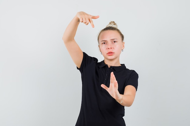 彼女の手を指している黒いTシャツを着た金髪の女性が伸びて真剣に見える、正面図。