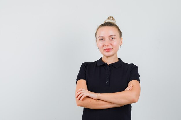 Blonde lady in black t-shirt standing with crossed arms and looking cheery , front view.