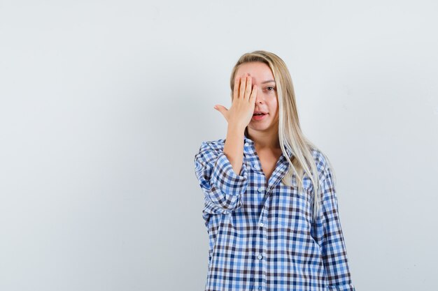 Blonde lady in casual shirt holding hand on eye and looking positive