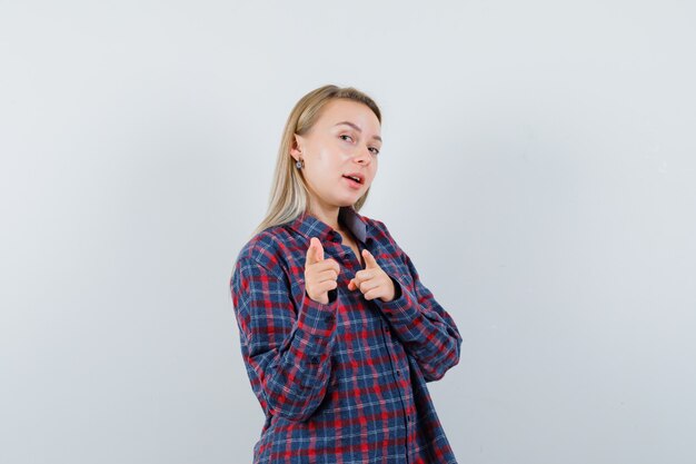 Blonde lady in casual shirt pointing at camera and looking confident , front view.