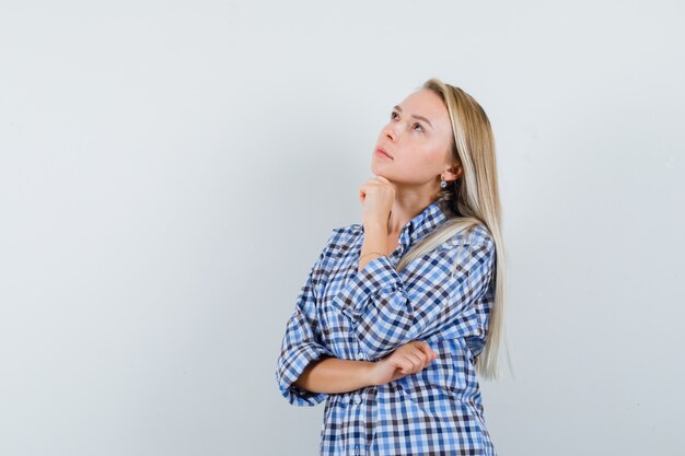 Blonde lady in casual shirt propping chin on hand and looking thoughtful