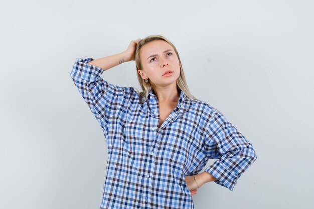 Signora bionda in camicia casual grattandosi la testa e guardando pensieroso