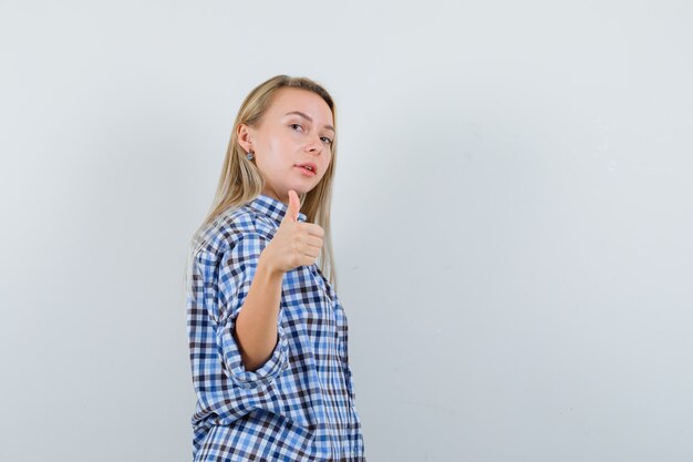 Blonde lady in casual shirt showing thumb up and looking confident .