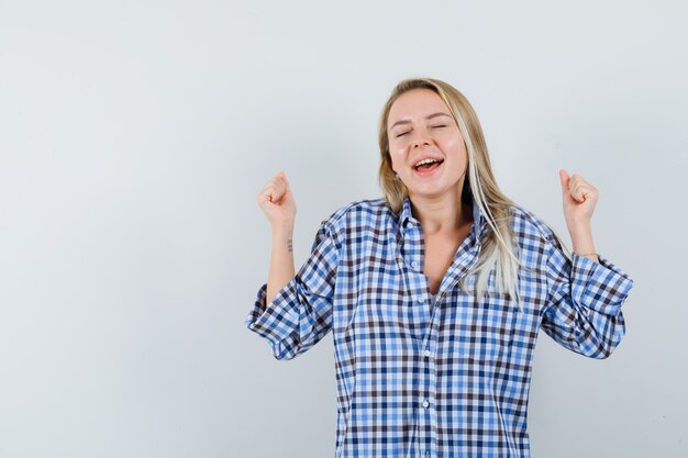 Blonde lady in casual shirt showing winner gesture and looking happy