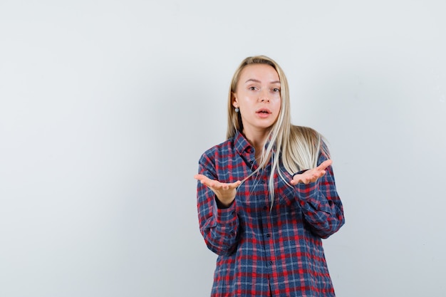 Signora bionda in camicia casual che allunga le mani nel gesto perplesso, vista frontale.