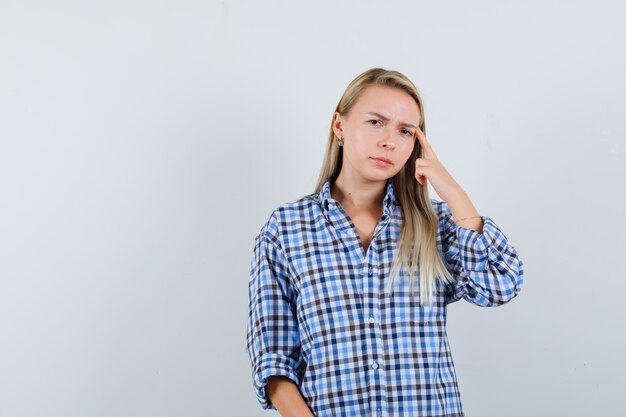Blonde lady in checked shirt holding finger on temples and looking thoughtful