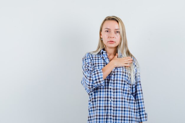 Blonde lady in checked shirt holding hand on heart and looking confident