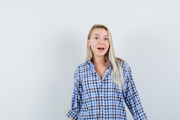 Blonde lady in checked shirt looking at camera and looking astonished