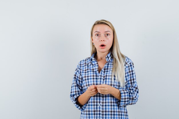 Blonde lady in checked shirt looking at camera and looking surprised