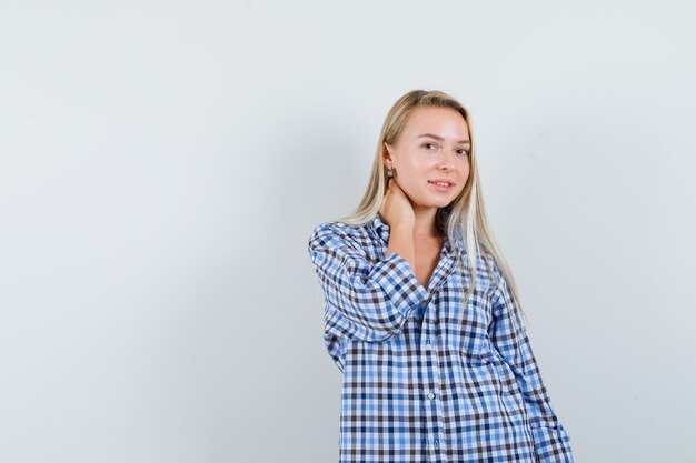 Blonde lady in checked shirt posing with hand on neck and looking pretty 