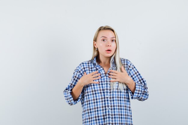 Blonde lady in checked shirt showing herself in questioning gesture and looking perplexed