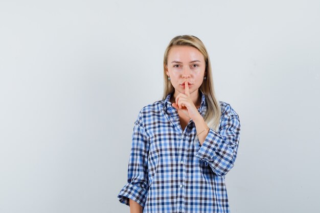Blonde lady in checked shirt showing silence gesture and looking confident