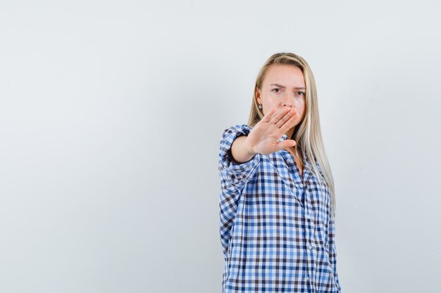 Blonde lady in checked shirt showing stop gesture and looking serious