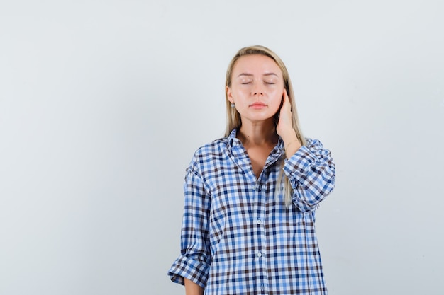 Blonde lady in checked shirt touching face skin on her cheek and looking relaxed