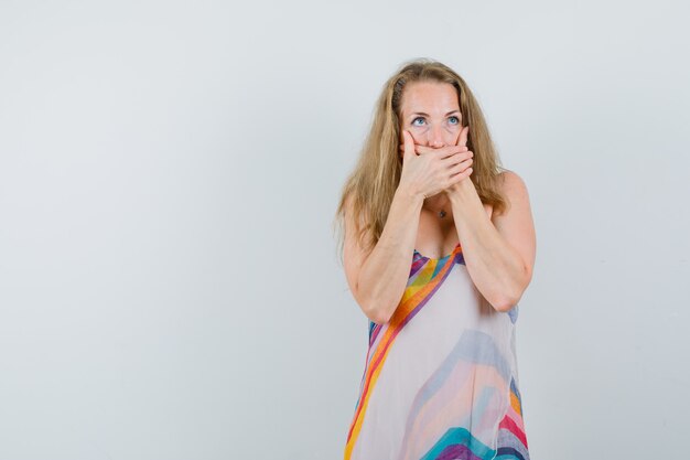 Blonde lady covering mouth with hands in summer dress and looking shocked 