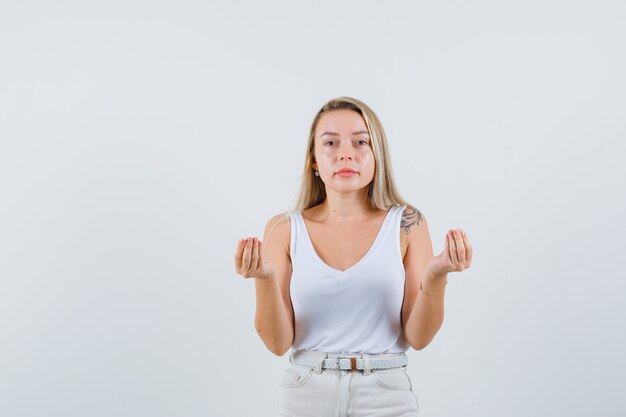 Blonde lady doing Italian gesture in singlet, pants and looking calm