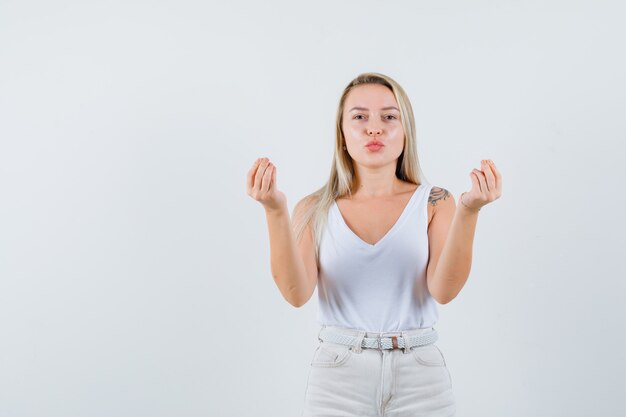 Blonde lady doing money gesture, pouting lips in singlet, pants and looking jolly