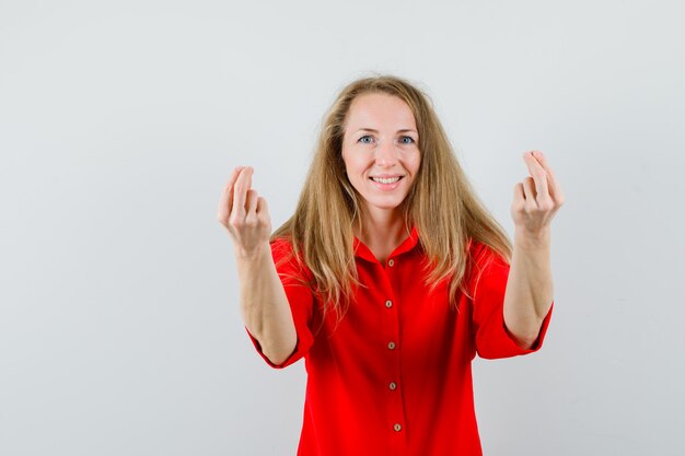 Blonde lady doing money gesture in red shirt and looking jolly ,