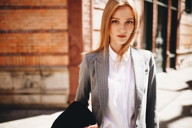 Blonde lady in grey suit enjoys the sunshine on the bright street of New York city