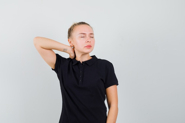 Blonde lady having neck pain in black t-shirt and looking tired , front view.