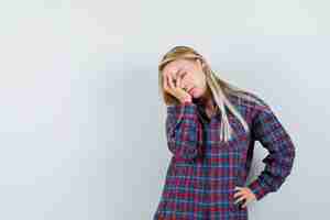 Free photo blonde lady holding hand on face in casual shirt and looking sleepy , front view.