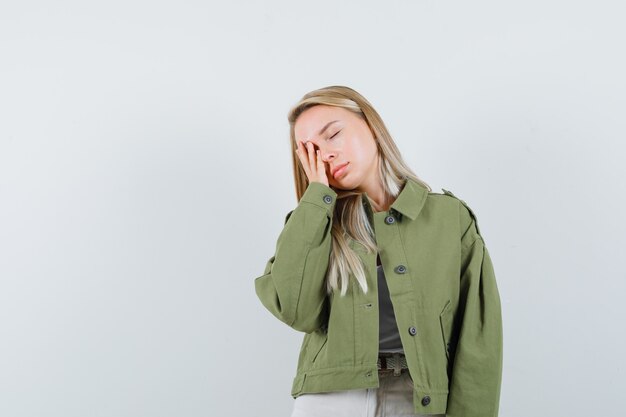 Blonde lady holding hand on face in jacket, pants and looking tired , front view.