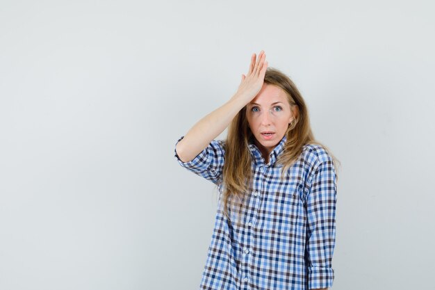 Blonde lady holding hand on forehead in shirt and looking puzzled ,