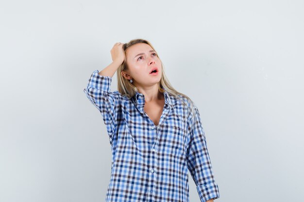 Blonde lady holding hand on head in checked shirt and looking puzzled