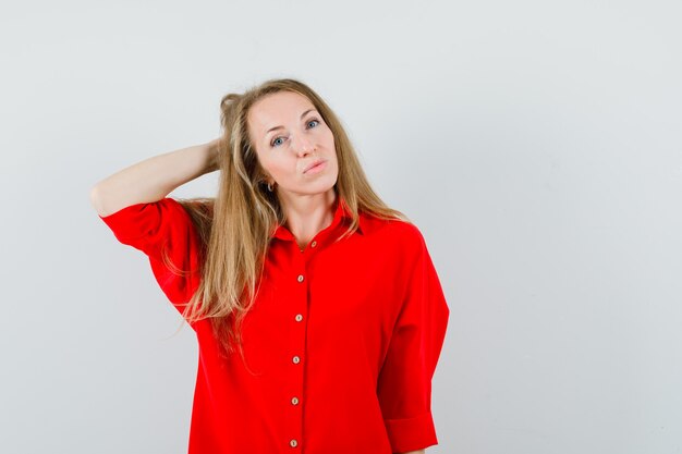 Blonde lady holding hand behind head in red shirt and looking pretty.