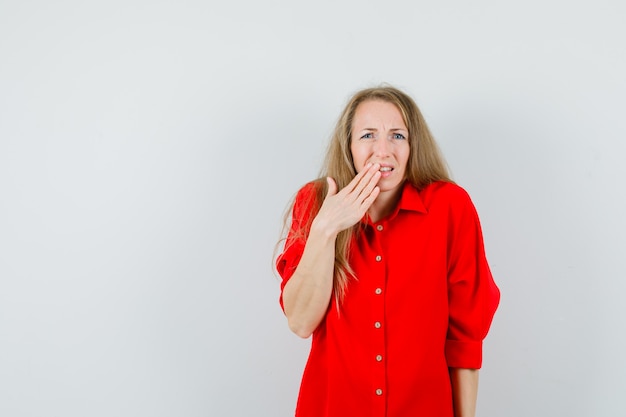 Blonde lady holding hand on mouth in red shirt and looking sorry.