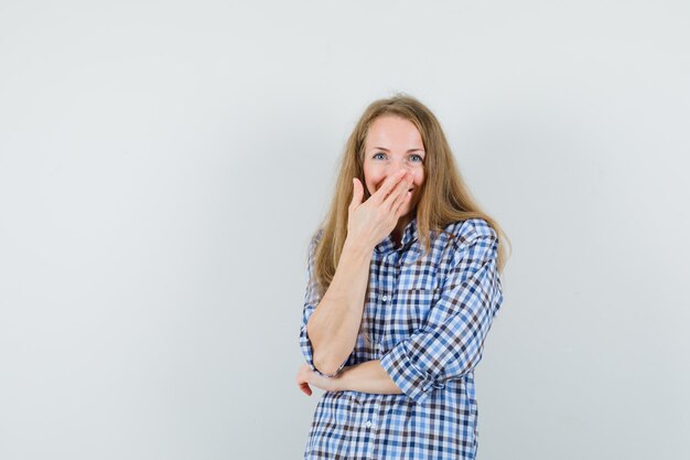 Blonde lady holding hand on mouth in shirt and looking joyful.