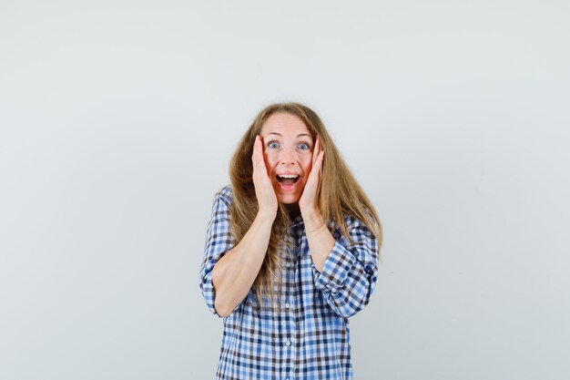 Blonde lady holding hands on cheeks in shirt and looking happy ,