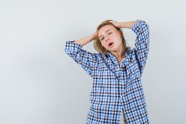 Blonde lady holding hands on head in casual shirt and looking delicate