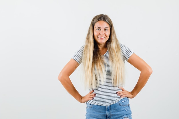 Free photo blonde lady holding hands on his waist in t-shirt and looking joyful. front view.