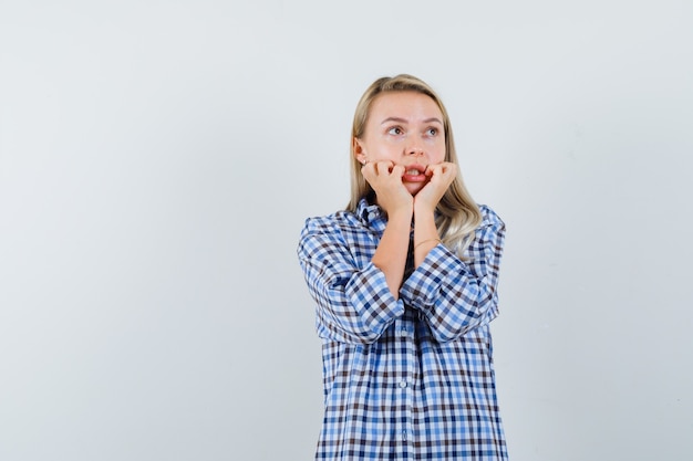 Free photo blonde lady holding hands near mouth in checked shirt and looking excited