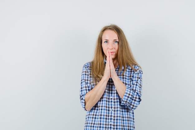 Blonde lady holding hands in praying gesture in shirt and looking sensible ,