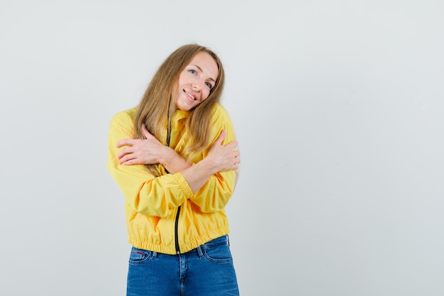 Blonde lady hugging herself in jacket, jeans and looking cute.