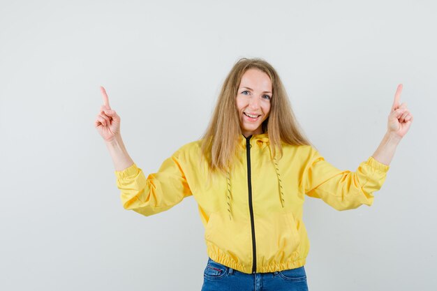 Blonde lady in jacket, jeans pointing up and looking cheerful ,