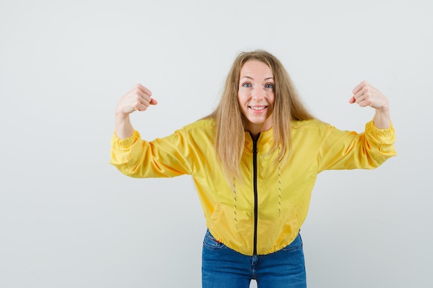 Blonde lady in jacket, jeans showing winner gesture and looking happy ,