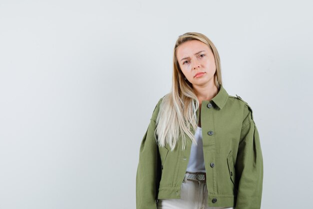 Blonde lady in jacket, pants looking at camera and looking upset , front view.