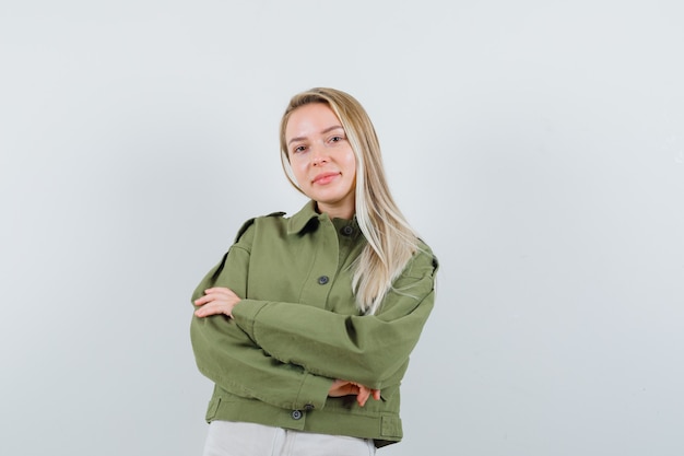 Blonde lady in jacket, pants standing with crossed arms and looking cheerful , front view.