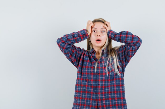 Blonde lady keeping hands on head in casual shirt and looking helpless. front view.