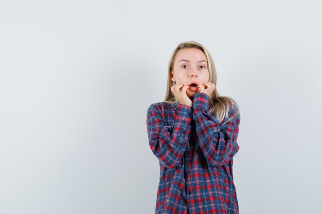 Blonde lady keeping hands near mouth in casual shirt and looking scared. front view.