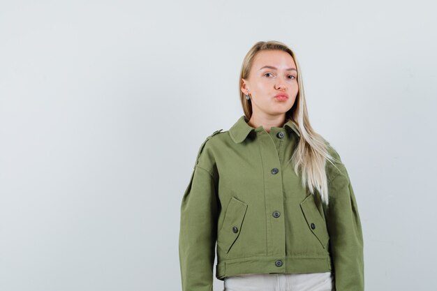 Blonde lady keeping lips folded in jacket, pants and looking pretty. front view.